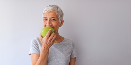 Ältere Frau beißt in einen grünen Apfel